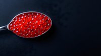 Fresh red caviar in silver spoon on dark background, luxury seafood delicacy with glossy texture and vibrant color, gourmet appetizer presentation.