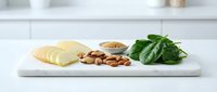 Fresh ginger root slices with almonds, sesame seeds and green basil leaves arranged on white marble cutting board in modern kitchen setting.