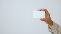 Cropped view of male hand holding blank white card against neutral background, suitable for business presentations, marketing materials, and promotional designs.