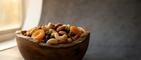 Wooden bowl filled with mixed nuts and dried fruits on kitchen counter near window with natural lighting for healthy snacking and cooking ingredients.