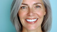 Mature woman with silver gray hair and bright genuine smile against blue background showcasing natural aging and confidence in healthcare and lifestyle advertising.
