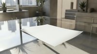 Modern minimalist white dining table with chrome legs in contemporary kitchen interior with stainless steel appliances and natural light from windows.