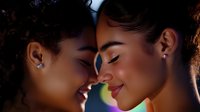 Close up portrait of young African American women with glowing skin and natural makeup smiling with eyes closed in intimate emotional moment against dark background.