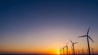 Wind turbines silhouetted against dramatic sunset sky with orange and purple hues. Renewable energy concept for sustainable power generation and environmental themes.