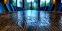 Rustic wooden table surface with natural grain texture in dark restaurant interior, dramatic lighting and blue chairs in background, shallow depth of field.