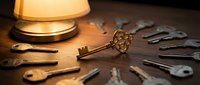 Vintage ornate brass key standing upright among scattered old keys on wooden surface with warm lamp lighting creating nostalgic locksmith workshop atmosphere.