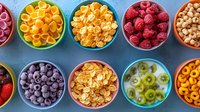 Colorful bowls filled with breakfast cereals, fresh berries and sliced fruits arranged in neat rows on blue background, top view flat lay composition.