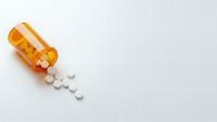 Orange prescription bottle spilled with white pills on clean background for healthcare and pharmaceutical concepts.