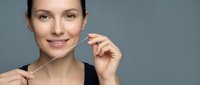 Young woman with fair skin and dark hair using dental floss for oral hygiene and teeth cleaning routine against neutral background.