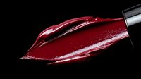 Luxurious red lipstick smear with silver tube on black background showcasing rich burgundy color and creamy texture for cosmetic advertising.