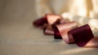 Elegant burgundy satin ribbon curled gracefully on neutral surface with soft natural lighting creating warm shadows and highlights for luxury packaging design.