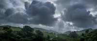 Dramatic storm clouds gather over lush green rolling hills and dense forest vegetation, creating moody atmospheric conditions ideal for nature, weather, and landscape design projects.