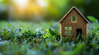 Small glittering house model placed in green grass with natural bokeh background, representing eco-friendly living, real estate, or sustainable home concept.
