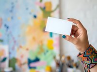 Hand holding blank white business card against colorful abstract wall background. Mockup for branding, marketing, and corporate identity presentation.