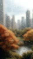 Blurred cityscape view through rain-covered window with autumn foliage in foreground, creating moody atmospheric scene with urban skyline and water droplets.