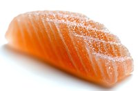 Fresh raw salmon fillet slice with visible texture and light coating of sea salt on white background, macro photography showing culinary detail.