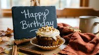 Autumn birthday cupcake with cream frosting and walnuts beside a chalkboard sign, cinnamon sticks, fall leaves, and a cozy mug.