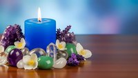 Blue candle burning surrounded by healing crystals, lavender flowers and jasmine blossoms on wooden surface for meditation, aromatherapy and wellness practices.