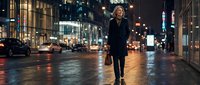 Professional blonde businesswoman walking on wet city street at night with briefcase and urban lights reflecting on pavement for corporate lifestyle concepts.