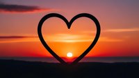 Heart-shaped frame silhouette against vibrant sunset sky with warm orange and pink colors creating romantic atmosphere for love concepts.