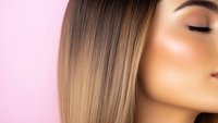 Close up profile view of young woman with straight blonde ombre hair and natural makeup against pink background, showcasing modern beauty and hairstyling trends.