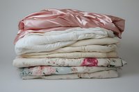 Stack of folded vintage bedding with pink satin, cream cotton, and floral pattern fabrics on neutral background, showcasing textile textures.