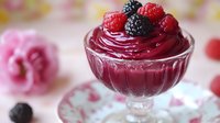 Fresh raspberry and blackberry mousse served in crystal dessert glass with pink floral background, sweet gourmet treat for romantic occasions and celebrations.