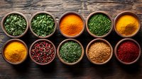 Colorful aromatic spices and herbs in wooden bowls on rustic table background, including turmeric, paprika, parsley, curry powder and pink peppercorns.