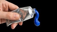 Tube of blue paint being squeezed out by hand with visible tattoo on skin, isolated on transparent background. Ready for design use on t-shirts, clipart, stickers, print-on-demand products, and sublimation projects.