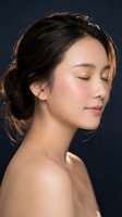 Young Asian woman with closed eyes and natural makeup in serene profile pose against dark blue background for beauty and wellness concepts.
