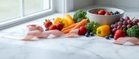 Fresh colorful fruits and vegetables arranged on marble kitchen counter near window with natural light for healthy eating and nutrition concepts.