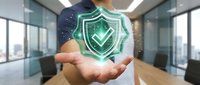 Businessman holding glowing green cybersecurity shield with checkmark in modern office environment representing data protection and digital security solutions.