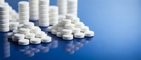 White pharmaceutical tablets and pills scattered on reflective blue surface for medical healthcare and medication concepts.
