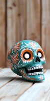 Decorative turquoise sugar skull with orange and white floral patterns on wooden background, traditional Mexican folk art celebration symbol for Day of Dead.