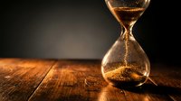 Golden sand hourglass on wooden table with dramatic lighting symbolizing time passage, deadlines, and life concepts for business presentations.