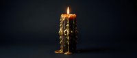 Melting wax candle with dripping sides and glowing flame against dark background creates atmospheric mood lighting for relaxation and meditation concepts.