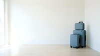 Set of three blue-gray hardshell suitcases stacked in a bright minimalist white room with wooden floor, ready for travel.