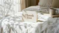 Thank you card on a cozy bed with white linen, soft morning light and shadows, warm neutral tones, minimalist bedroom setting.