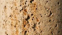 Close-up of rough sandy stone surface with natural pores and warm earthy tones, shallow depth of field highlighting texture detail.