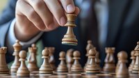 Business professional making strategic move with wooden chess piece on board, demonstrating leadership and decision making in competitive environment.