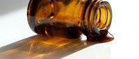 Amber glass bottle tipped over spilling liquid on white surface with dramatic shadow, suitable for healthcare, pharmaceutical, and wellness product marketing.