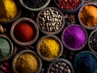 Vibrant colorful spices and herbs in rustic bowls, including turmeric, paprika, pepper, and exotic seasonings arranged on dark wooden surface.