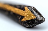Macro shot of black pencil tip with golden arrow symbol, showing texture and detail against white background, selective focus creates artistic depth of field effect.