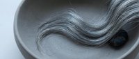 Gray hair strand flowing in white ceramic bowl, hair care and aging concept for beauty salon treatments and anti-aging products marketing materials.