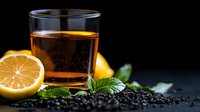 Fresh glass of tea with lemon slices and mint leaves on dark background with scattered black peppercorns, moody food photography composition.