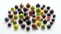Assorted fresh figs in various stages of ripeness, including whole fruits and halved specimens displaying pink flesh, arranged on white background for culinary and food styling use.