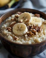 Creamy rice pudding topped with fresh banana slices and crunchy walnuts in rustic wooden bowl, comfort food styling for breakfast or dessert recipes.