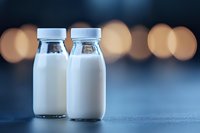 Fresh milk in glass bottles on dark background with soft bokeh lights, dairy product photography for healthy lifestyle and natural food concepts.