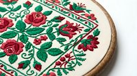 Traditional folk embroidery with red roses and green leaves in wooden hoop, handcrafted needlework art for home decor and cultural heritage projects.