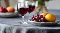 Red wine glasses with fresh fruits on gray linen tablecloth. Elegant table setting with grapes, oranges and apples creating cozy atmosphere for dining or celebration.